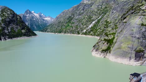 Luftdrohne-Vorwärtsbewegende-Aufnahme-über-Einem-Wasserfall-In-Der-Ferne-Entlang-Des-Grimselsees-In-Der-Nähe-Der-Grimselpass-Hochgebirgsstraße-In-Den-Wunderschönen-Schweizer-Alpen,-Schweiz-Bei-Tag