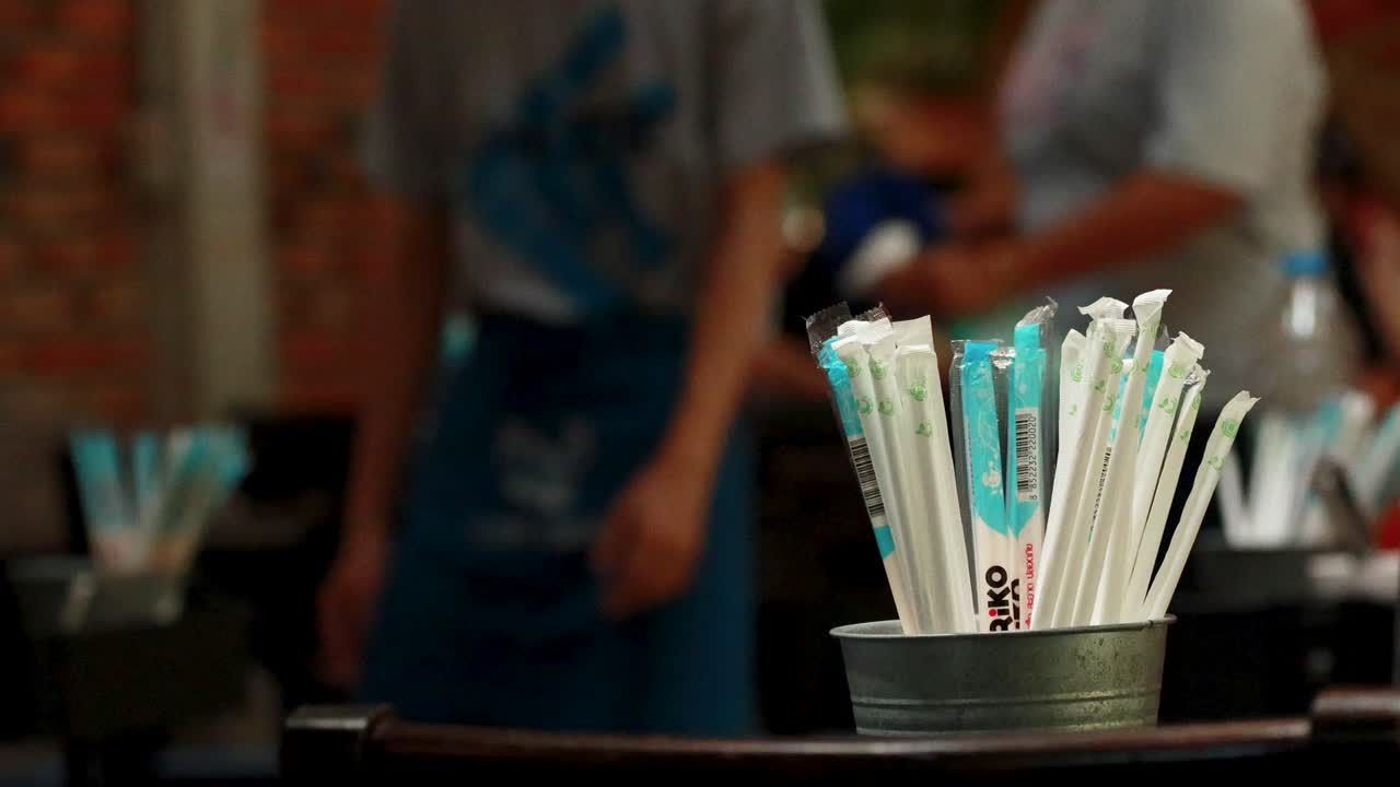 A collection of straws in a container at a restaurant in Phuket, Thailand, with blurred background activity and natural lighting