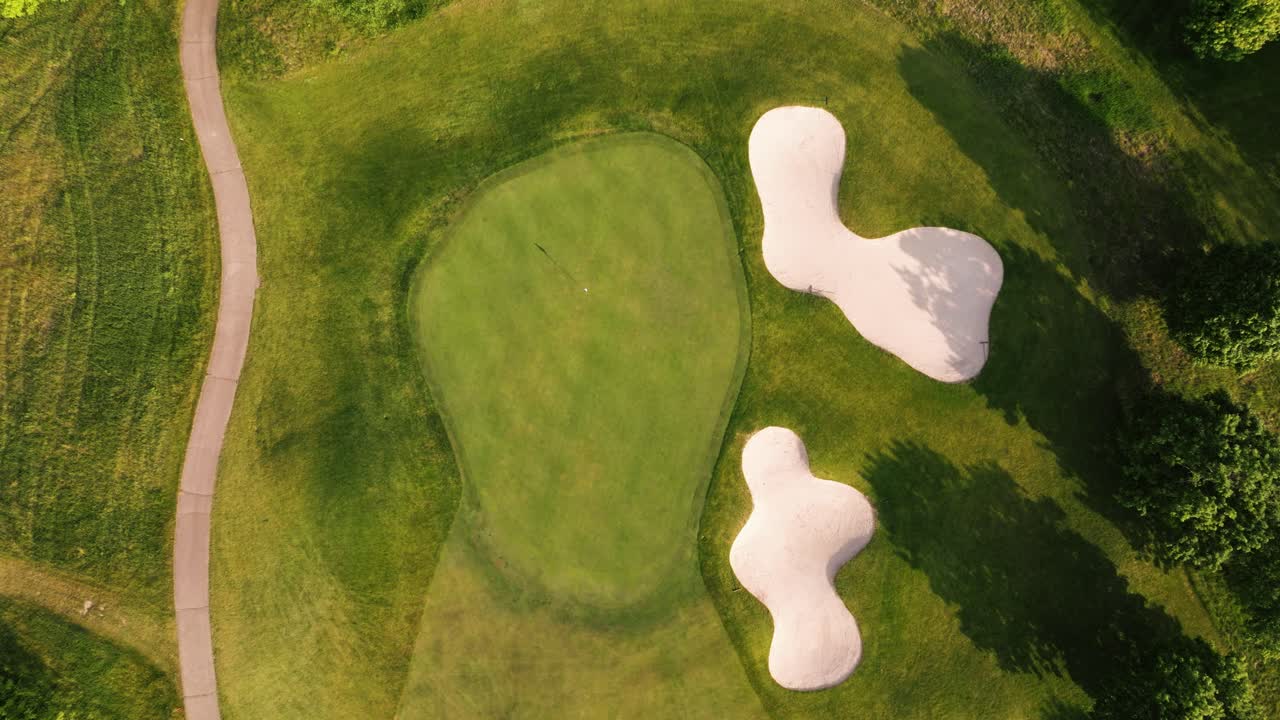 Aerial topdown overview descends on golf course hole with trimmed green and surrounding sand traps