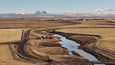 Aerial view of Iceland’s Þjórsá river winding through golden farmland under winter sunlight with snow-covered mountains.