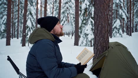 man reading a book in a snowy forest