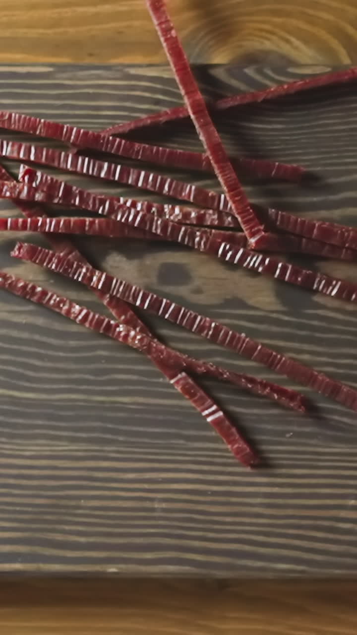 Person drops delicatessen jerked red fish sticks onto rustic wooden cutting board put on countertop in room close view from above slow motion