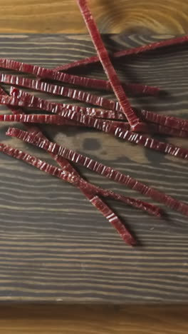 person drops delicatessen jerked red fish sticks onto rustic wooden cutting board put on countertop in room close view from above slow motion