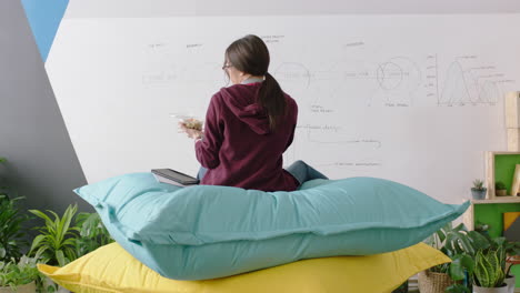 mujer de negocios feliz haciendo lluvia de ideas disfrutando del almuerzo comiendo relajándose en almohadas coloridas revisando mensajes de redes sociales en el teléfono inteligente en el lugar de trabajo moderno de la oficina