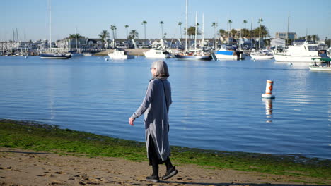 an active and healthy woman at retirement age with a walking stick for her disability waving to friends on the beach in newport, california on a sunny pleasant day