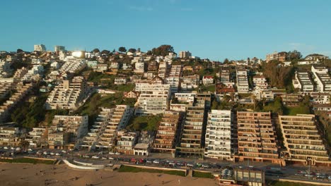 Aerial-view-left-across-Reñaca-coastal-city-buildings-on-Vina-Del-Mar-sunny-beach-resort-waterfront