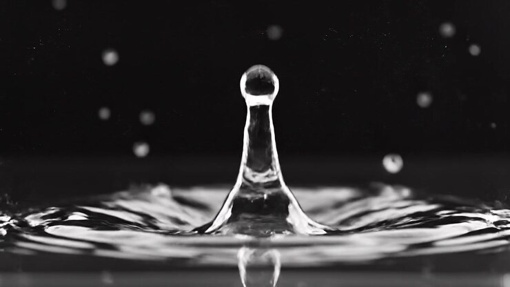 Scatto macro di una goccia di liquido trasparente che colpisce una superficie scura