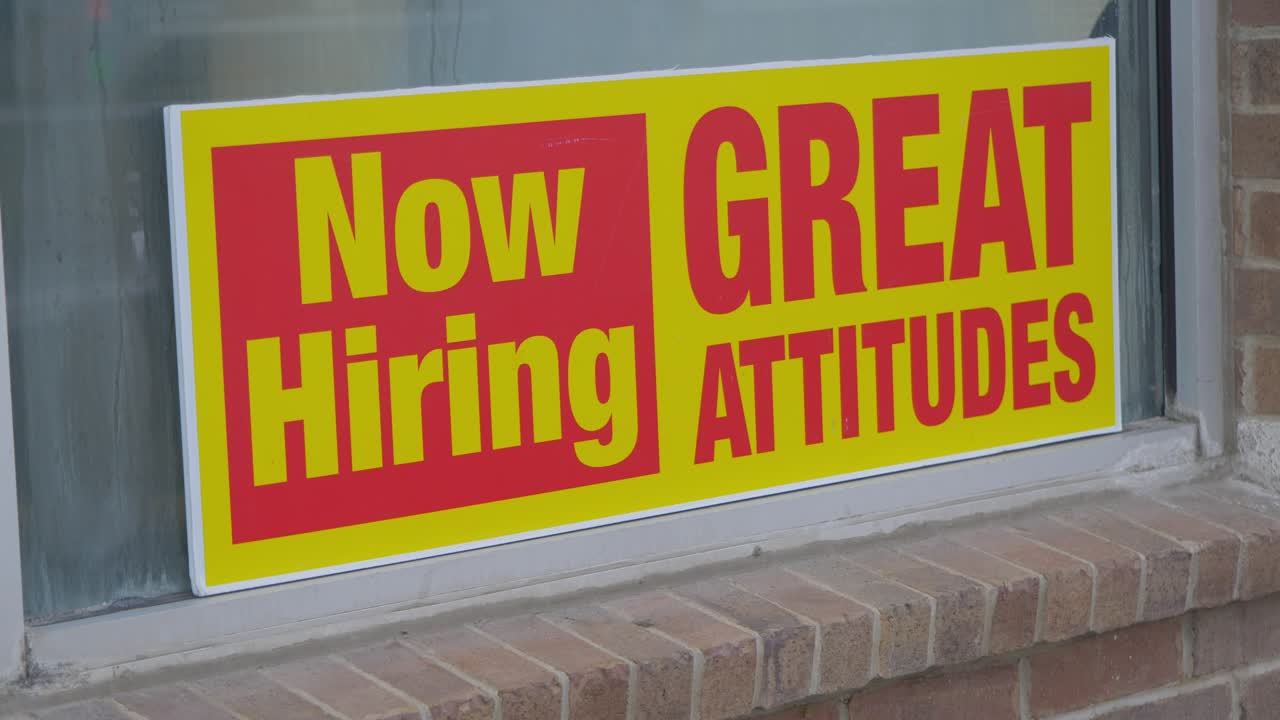 Now hiring great attitudes bright yellow and red sign in window of car wash with condensation dew on glass on brick wall, static close-up camera angle in Cinema 4K 30fps slowed from 60fps