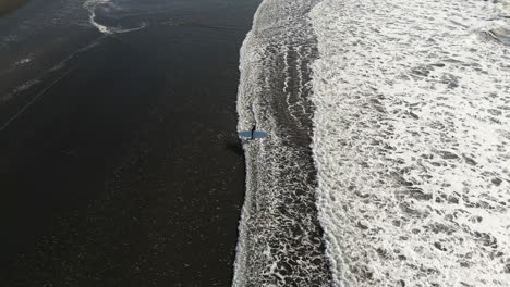 drone view of a surfer who enters the water, side view