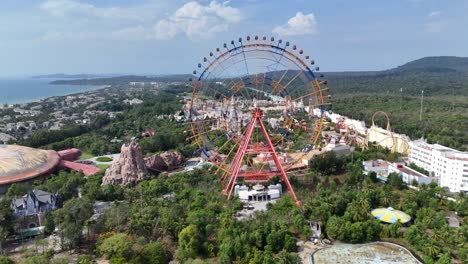 the aerial perspective amusement park, its colossal ferris wheel offering panoramic views of the coastline and ocean. teeming with themed structures and lush vegetation, the park has coastal hotels.