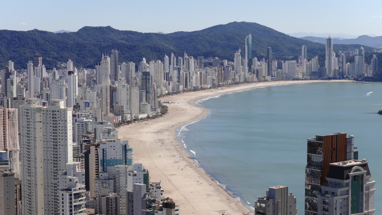 Drone slow gliding over Balneario Camboriu's coastline captures the vibrant cityscape, sandy beach, and expansive ocean, highlighting urban development and natural beauty