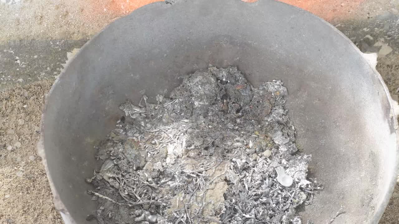 Piombo fuso mescolato in una pentola di metallo, fiamme che lambiscono la superficie, vista dall'alto