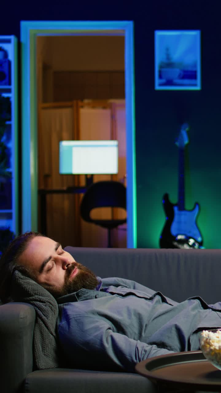 Vertical video Sleepy man struggling to stay awake on couch after working on laptop