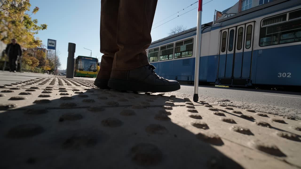 시각장애인 남자가 자신의 지이로 도로를 건너고 있는 모습이 도시에서 시각장애인을 위한 촉각적인 보행자 보행자 도로의 도움으로 보여진다.