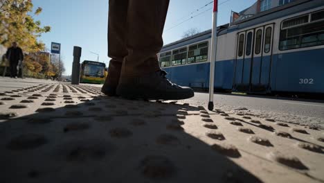 visually impaired man crossing the road with his stick with the help of tactile pedestrian sidewalk for the visually impaired in the city.