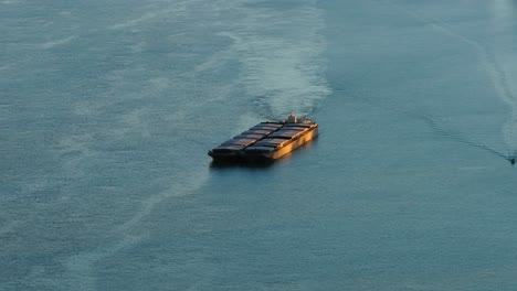 aerial close up shot pusher tug pushing barges on a big river, illuminated by sunlight, 4k50fps