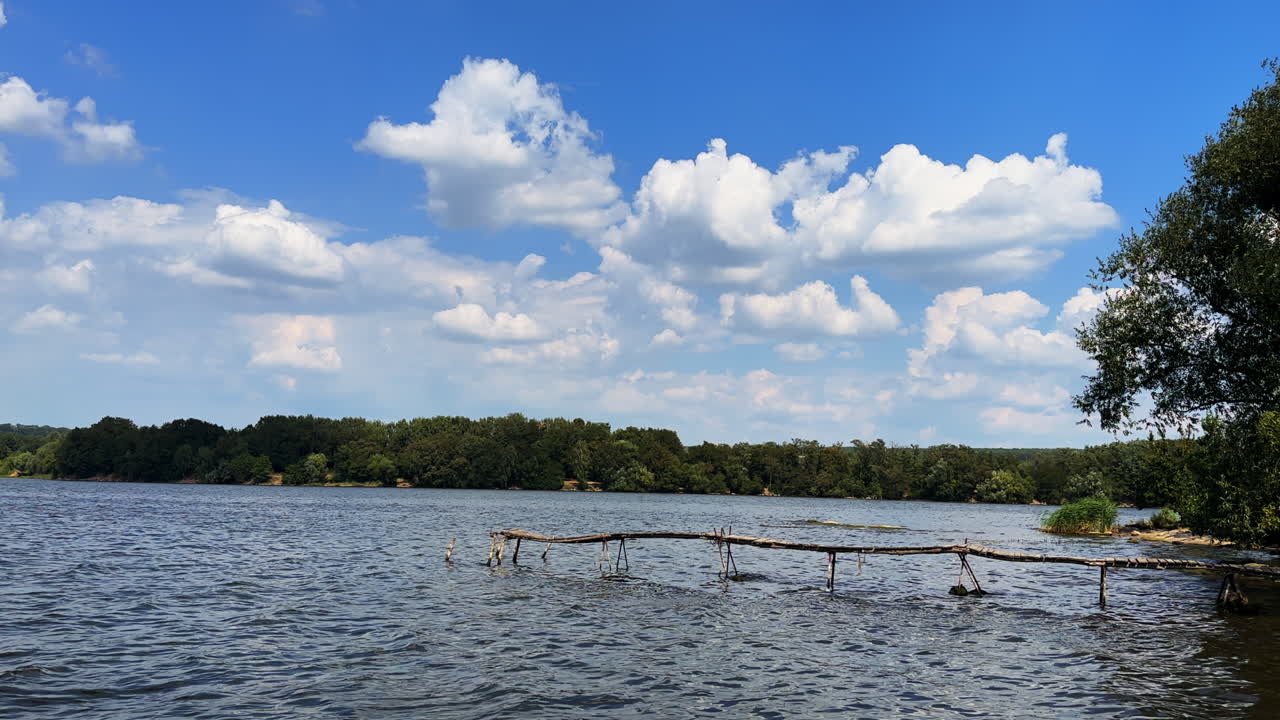 Water flowing quickly in the beautiful river. View on the Lovely waterscape with unsecure wooden bridge on. Summer sky with clouds at backdrop.