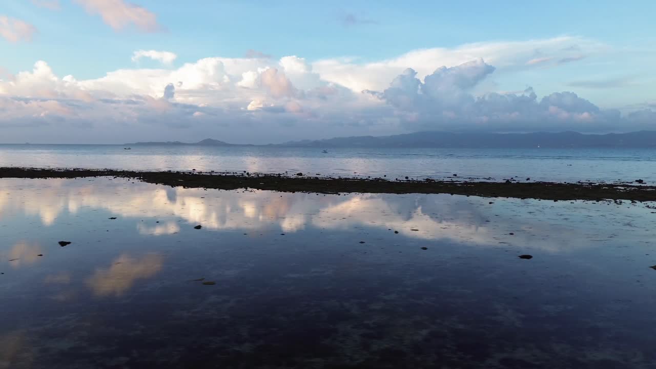 Drone footage of sunrise over Koh Phangan Thailand with a small boat moving across the calm tropical sea and the sunlight reflecting boat and clouds brightly on the water surface