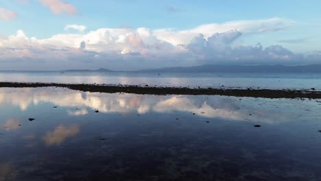 Drone footage of sunrise over Koh Phangan Thailand with a small boat moving across the calm tropical sea and the sunlight reflecting boat and clouds brightly on the water surface