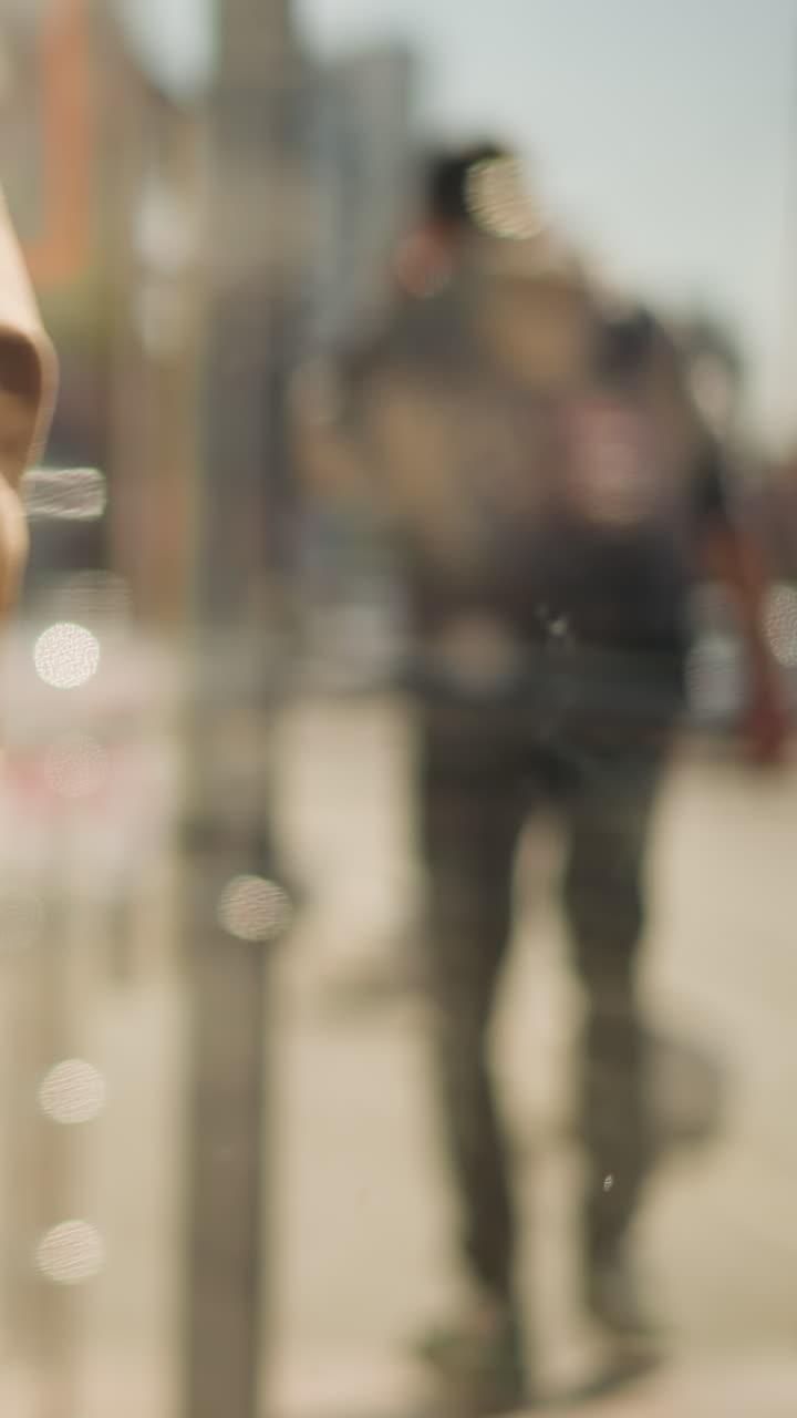 Manilla de puerta de cristal y marco de metal con un peatón borroso pasando al fondo, reflejos de la fachada de una tienda de la ciudad y cálida luz solar creando una atmósfera bokeh en capas, momento de pasaje urbano cinematográfico