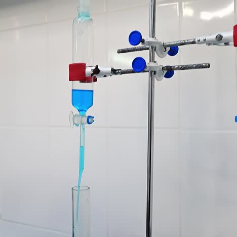 scientist pours blue liquid into reservoir. liquid goes to the glass tube right onto the diaper. researcher's hand holds the timer to check the time of absorbing