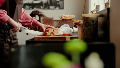 cerca de una foto en cámara lenta de una joven cocinera cortando pan recién hecho con un cuchillo en la cocina