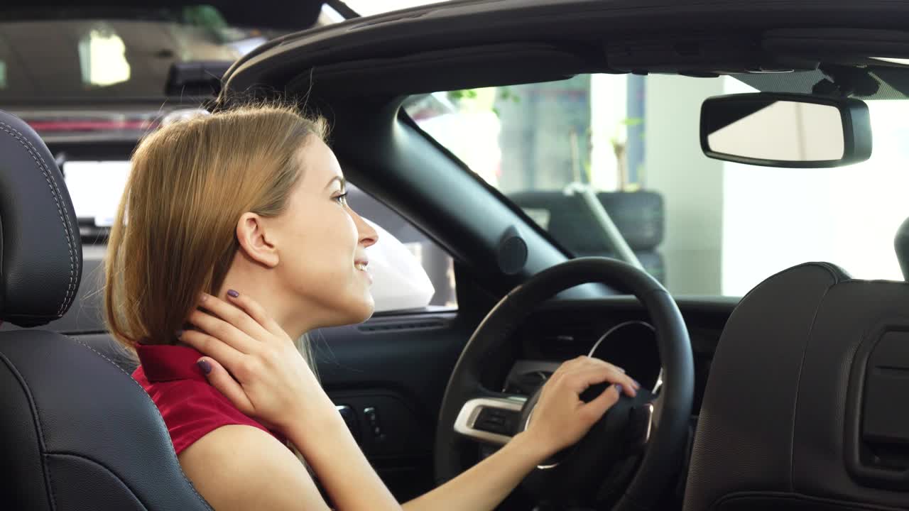 멋진 젊은 여성 운전자가 그녀의 컨버터블에 기게 웃고 앉아 있습니다.