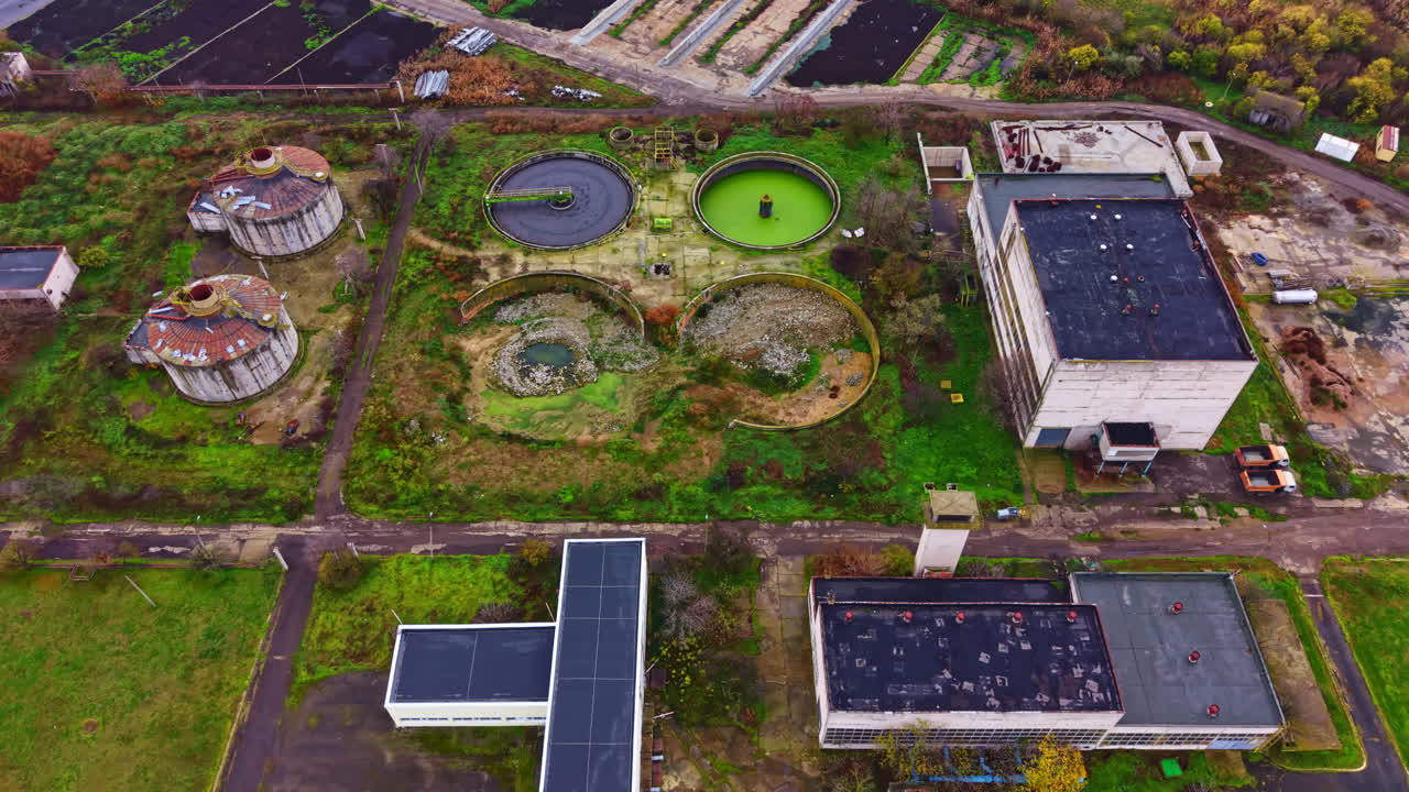 View of an abandoned industrial site with various structures and green spaces under a cloudy sky