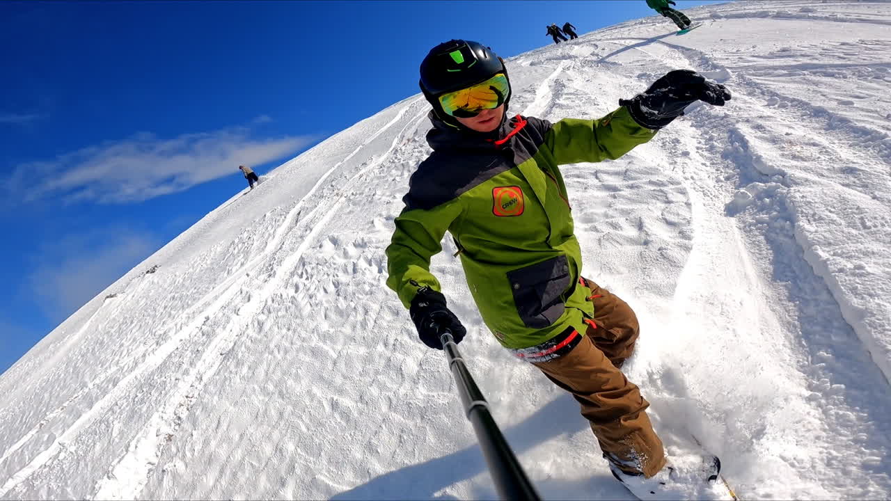 Man taking selfie as going down the slope. Snowboarders practicing on the snowy hill.