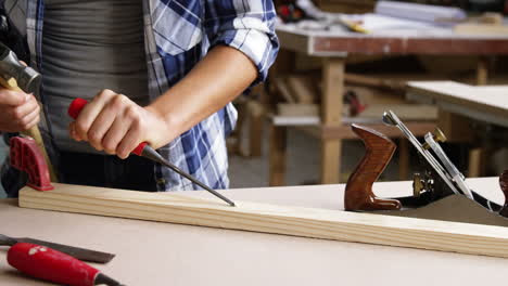 Focus-on-carpenter-using-hammer-and-chisel-on-wooden-plank