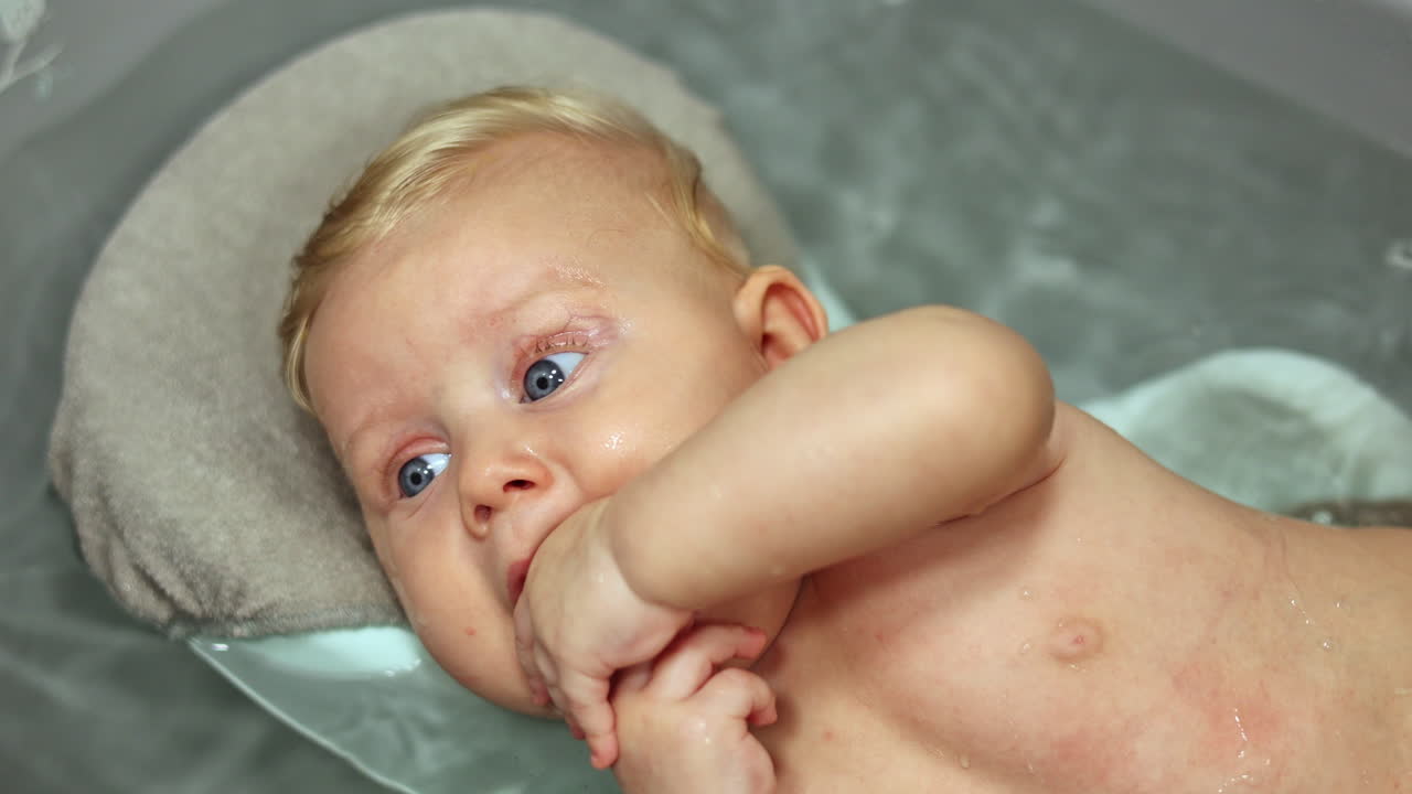 Bathing the baby in the bath while lying on the stand. Baby's first baths. Baby hygiene. A 3-month-old baby is lying in the bathroom