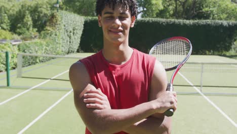 Portrait-of-happy-biracial-man-with-tennis-racket-in-garden-on-sunny-day