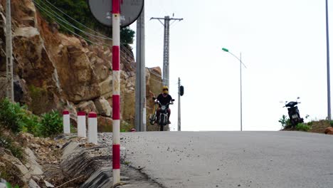 Man-On-A-Motorcycle-Carrying-Surfboard-On-Mountain-Road-In-Vinh-Hy,-Vietnam