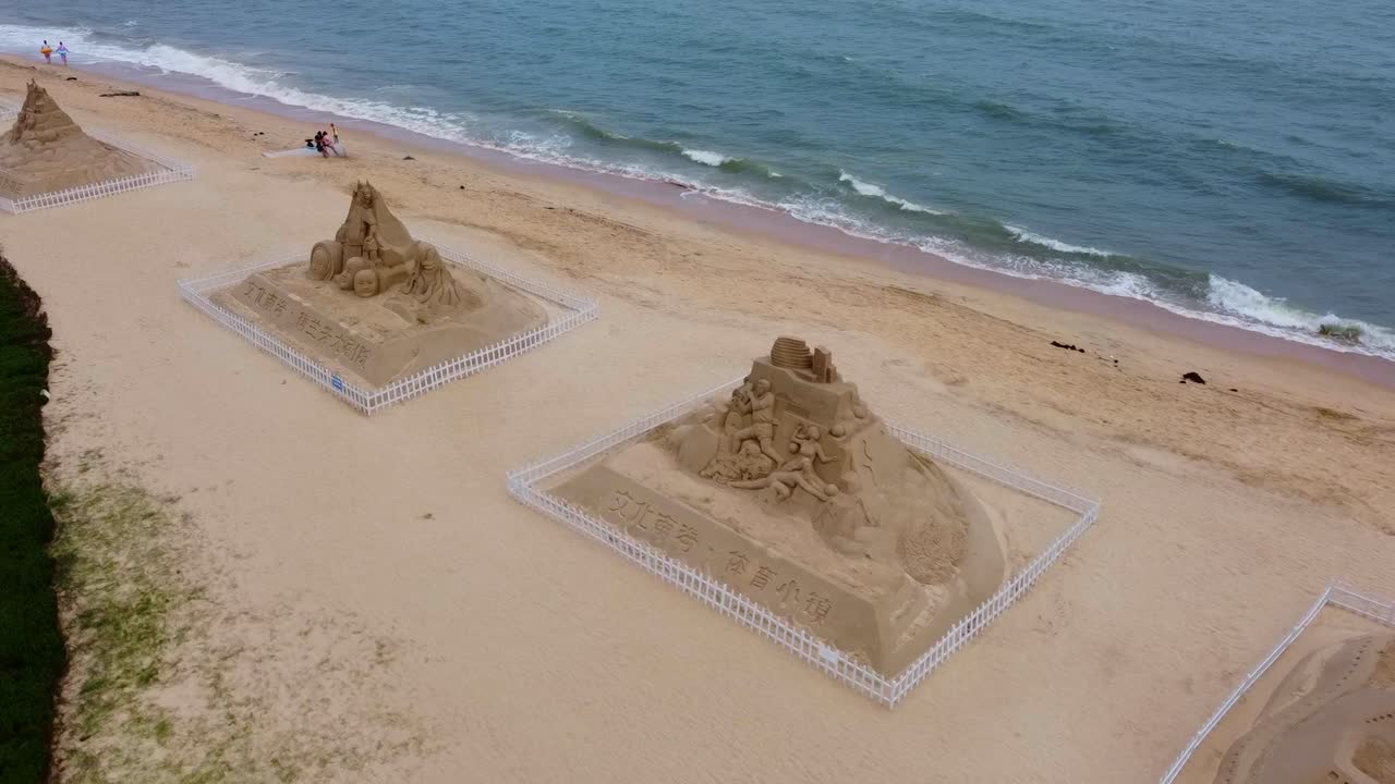 Low aerial closeup view of pyramid sand sculptures and castles on sandy beach with calm waves during summer