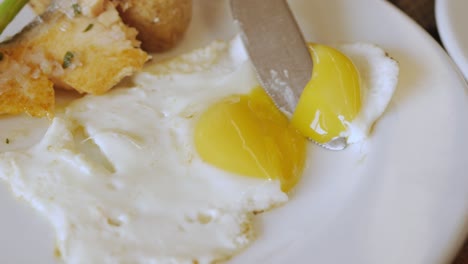 usar un cuchillo cortado y romper un huevo frito fresco en un plato para un desayuno saludable