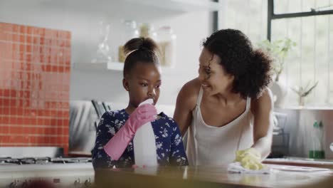 happy african american mother and daughter cleaning kitchen together, slow motion