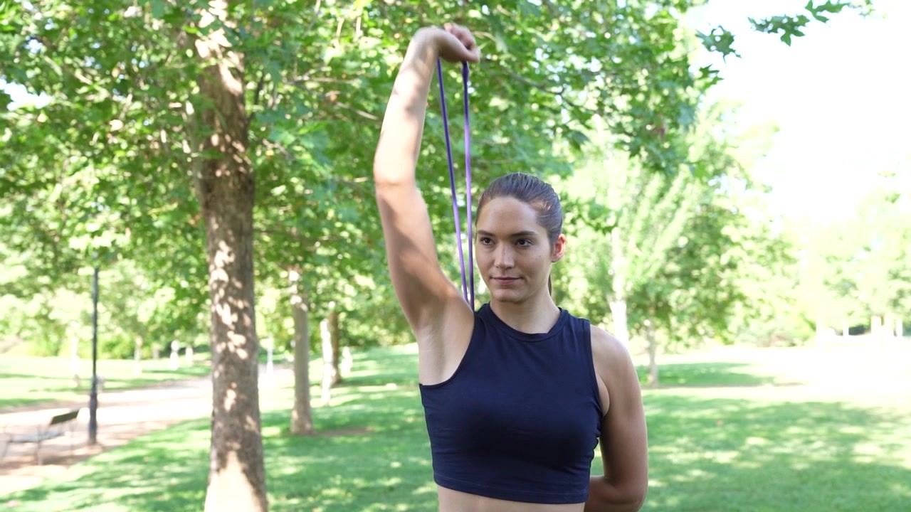 Una donna si allena con una fascia di resistenza in un parco, concentrandosi sull'allenamento e sulla natura circostante