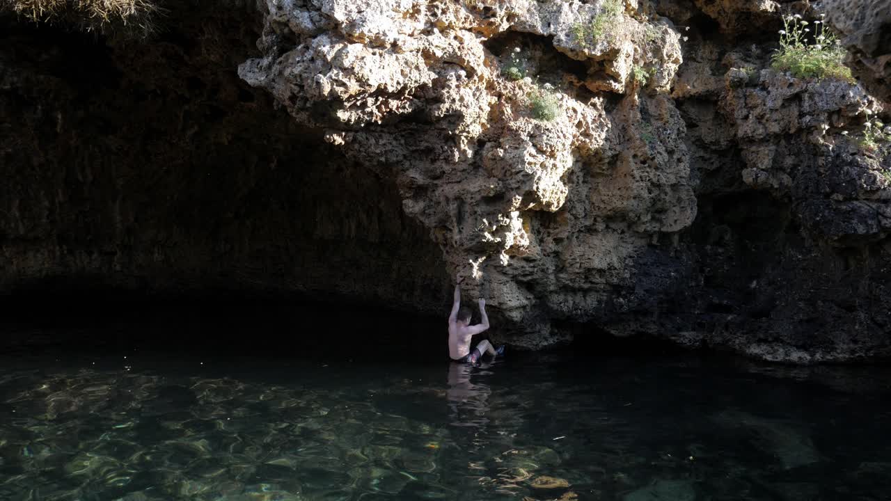 Man deep-water solo climbing on rugged limestone cliffs above clear water at Cala Rafaelet
