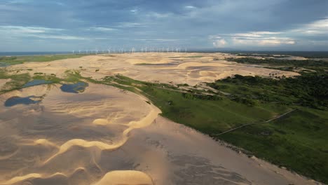 Wunderschöne-Drohnenaufnahme-Eines-Paradiesischen-Strandes-Inmitten-Der-Dünen-Und-Windkraftanlagen-Im-Hintergrund,-Sonnenuntergangslicht