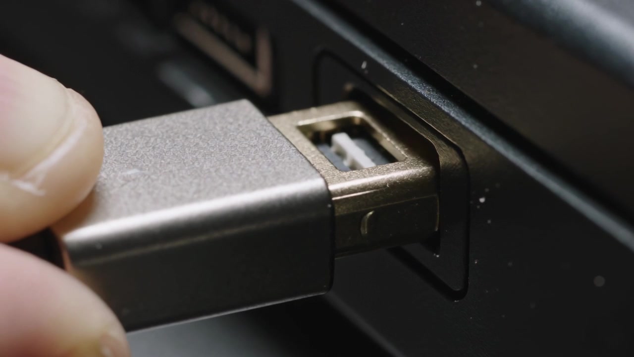 Positioning adult hand aligning USB connector, inserting into laptop side port, connecting device