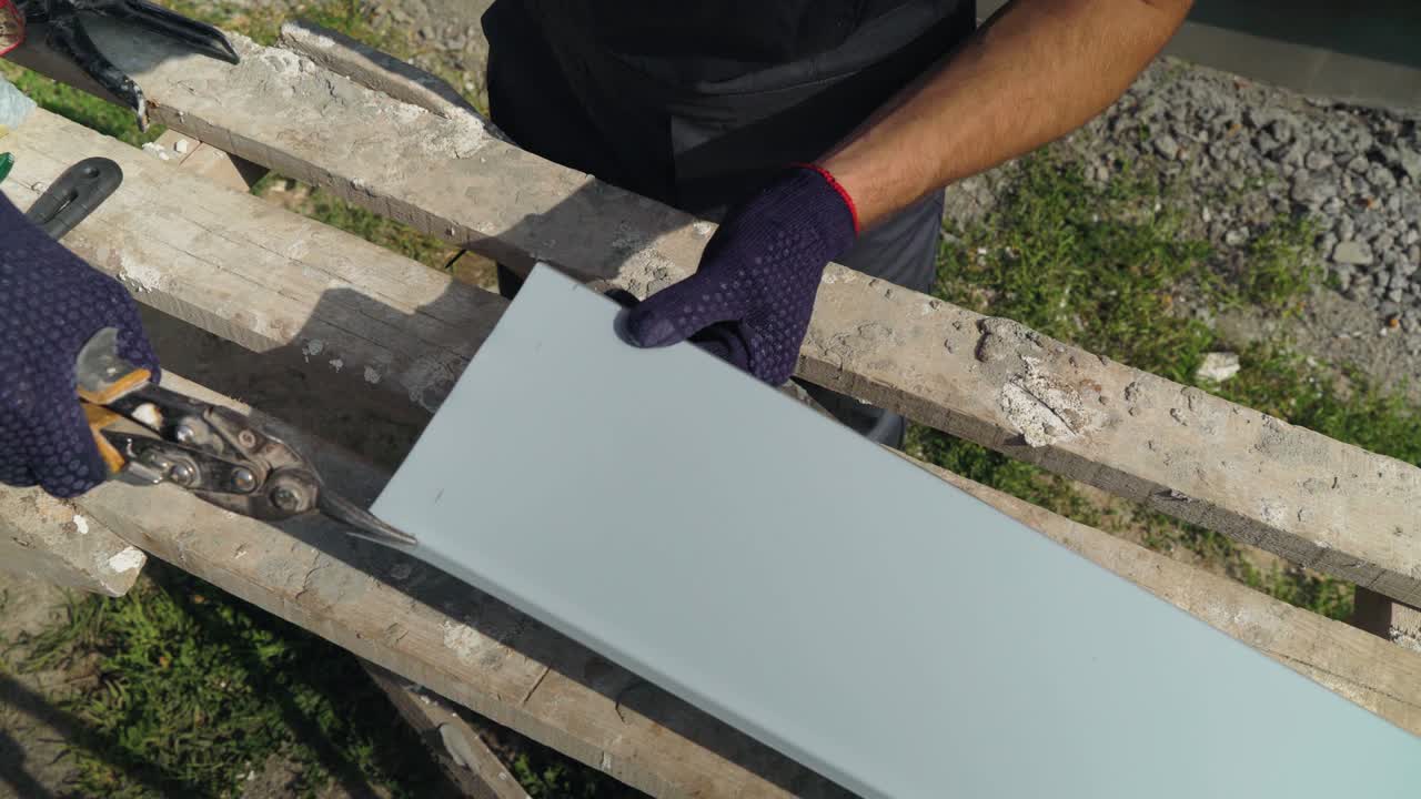 Primo piano delle mani di un operaio con guanti protettivi che prepara un davanzale in PVC tagliando il metallo con le forbici.