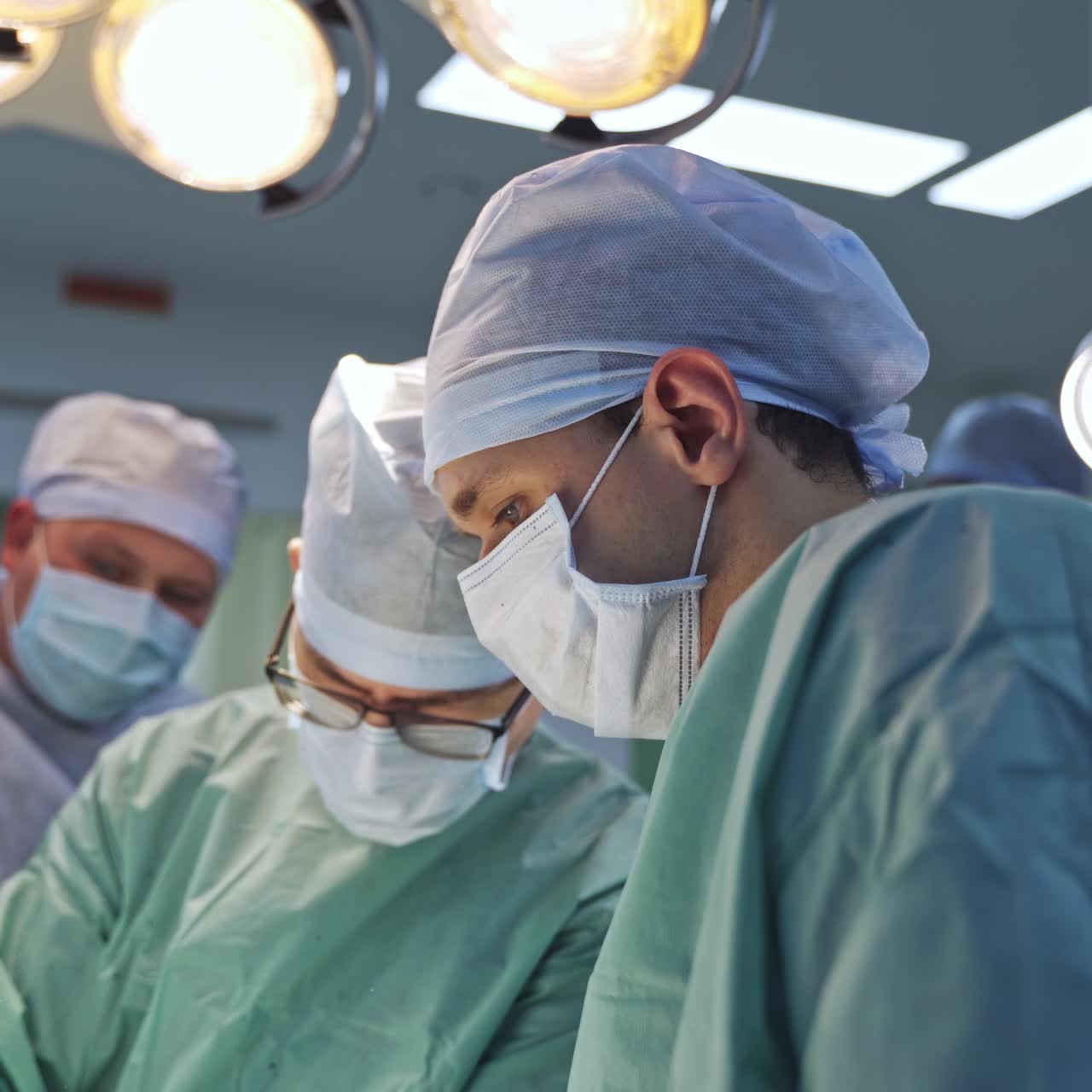 Equipo médico formado por varios doctores durante una operación. Cirujanos de sexo masculino de pie bajo las luces en un quirófano moderno. Concepto de atención médica