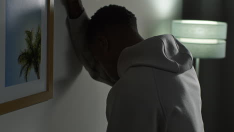 young man with mental health issues standing leaning against wall at home looking depressed and unhappy 1