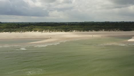 Schöne-Luftaufnahme,-Die-Sich-An-Einem-Bewölkten-Tag-über-Wellen-In-Richtung-Eines-Weißen-Strandes-Und-Einer-Grünen-Landschaft-Bewegt