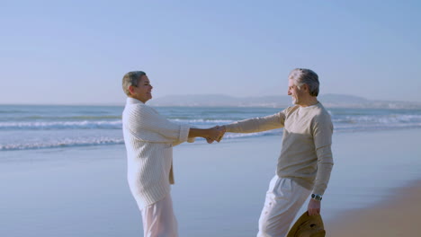 happy senior caucasian couple dancing and then hugging on the beach