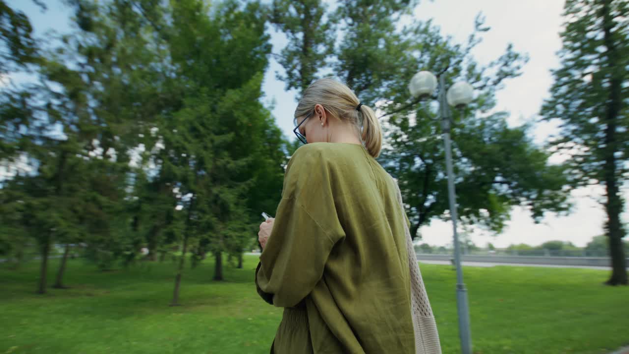 Frau, die in einem Park spaziert und ein Handy benutzt