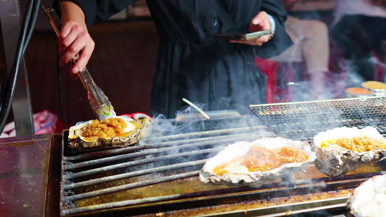 Oysters being grilled with flames and tongs