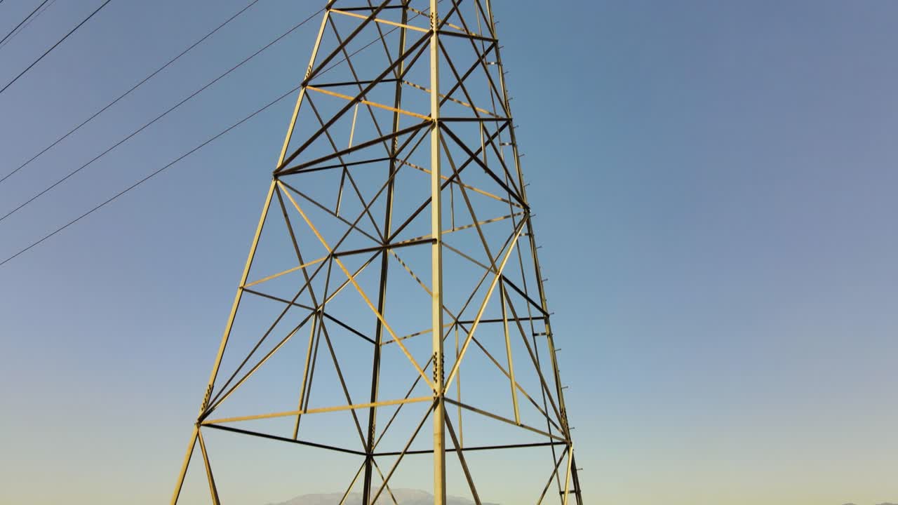 Drone ascends to capture a towering power line structure against the canvas of a clear, blue sky