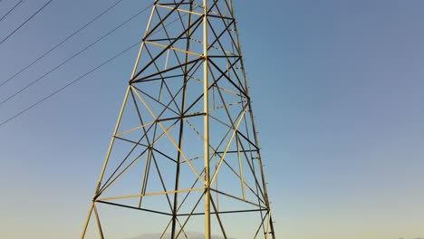 Drone-ascends-to-capture-a-towering-power-line-structure-against-the-canvas-of-a-clear,-blue-sky