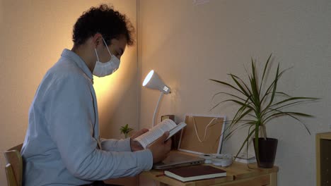 a man wearing facemask reading a book at his home office during the coronavirus outbreak - closeup shot